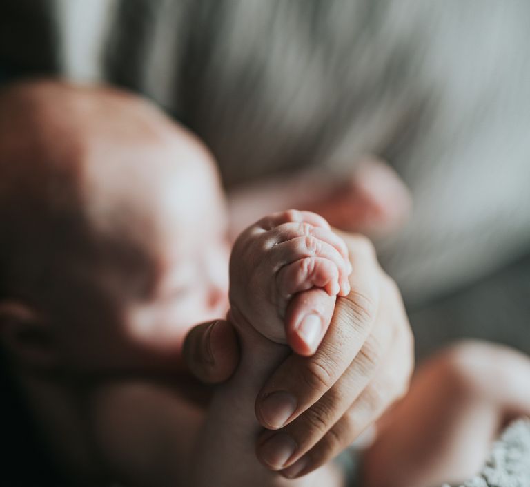 Kleine Babyhand umfasst den Finger einer erwachsenen Hand.